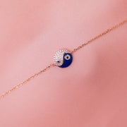 A sterling silver Yin-Yang charm bracelet with a rose gold finish and blue and clear accents on a pink background.